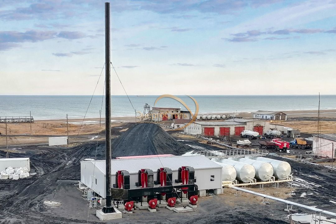 Полный вид котельной с четырьмя котлами КВм-1,16МВт, циклонными золоуловителями и дымовой трубой с растяжками. Комплекс обеспечивает тепло и ГВС прибрежному посёлку в арктической зоне.