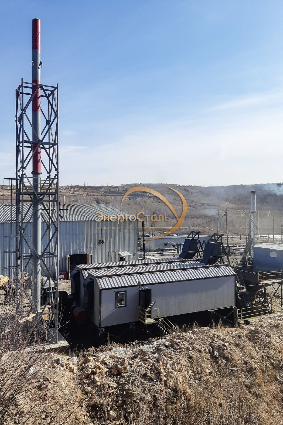 Общий вид на котельную: технологический блок, загрузочный узел топлива и решётчатая башня трубы. Схема «2×КВм-2,5МВт»: один котёл держит базу, второй — пик/резерв. Площадки и лестницы обеспечивают безопасный обход.