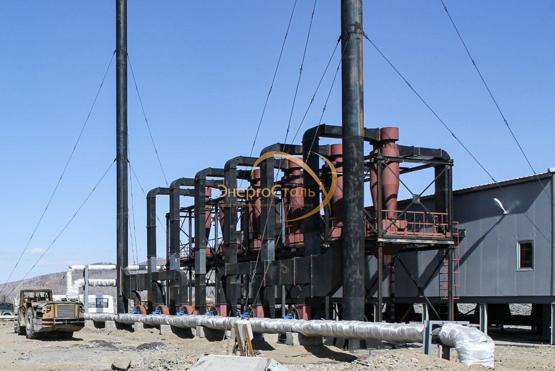 Крупные подающая/обратная линии, опоры и лестницы доступа. Разнесение трубопроводов под зданием упрощает ревизию арматуры и снижает теплопотери благодаря утеплённым боксам.