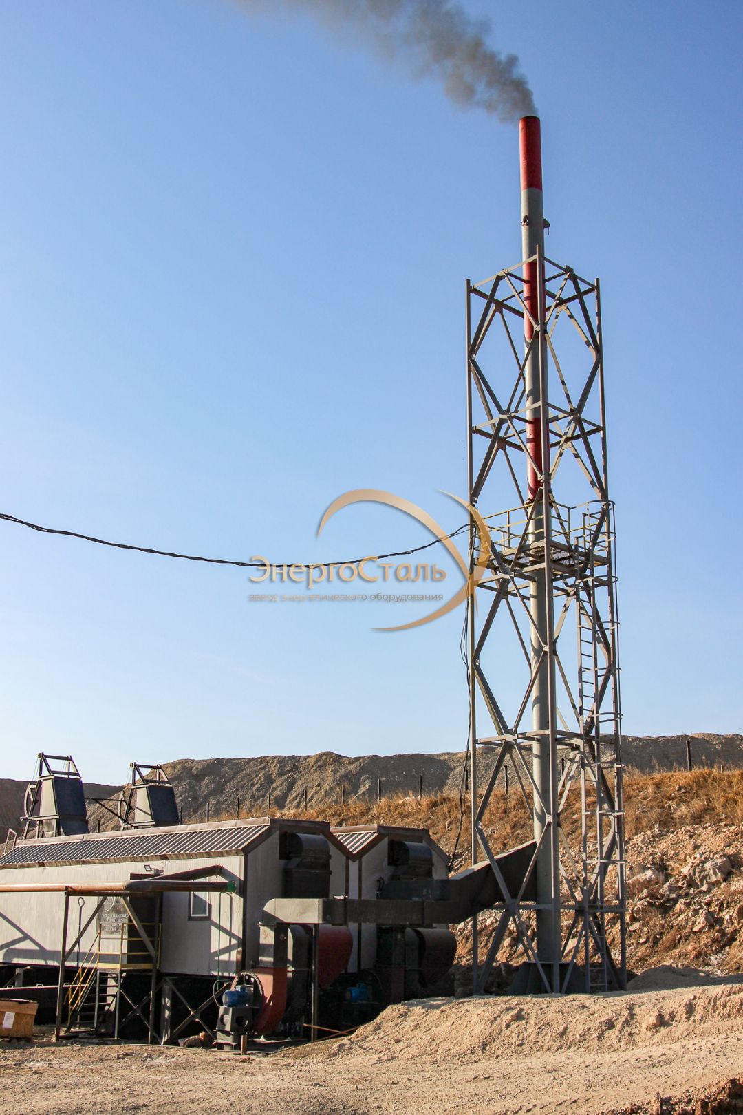 Решётчатая мачта с дымовой трубой и оголовком, система растяжек и опор. На заднем плане — котельный блок со скиповыми подъёмниками. Конфигурация рассчитана на непрерывную работу при