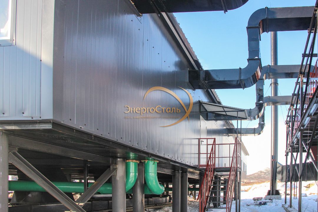 Крупные подающая/обратная линии, опоры и лестницы доступа. Разнесение трубопроводов под зданием упрощает ревизию арматуры и снижает теплопотери благодаря утеплённым боксам.